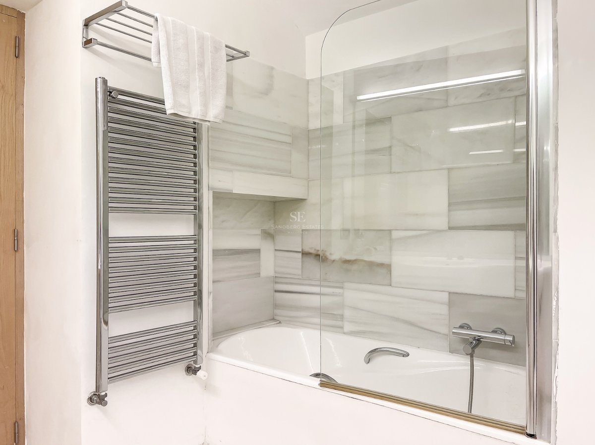 Baignoire blanche avec paroi en verre, carrelage mural en marbre gris et blanc et sèche-serviettes chromé.