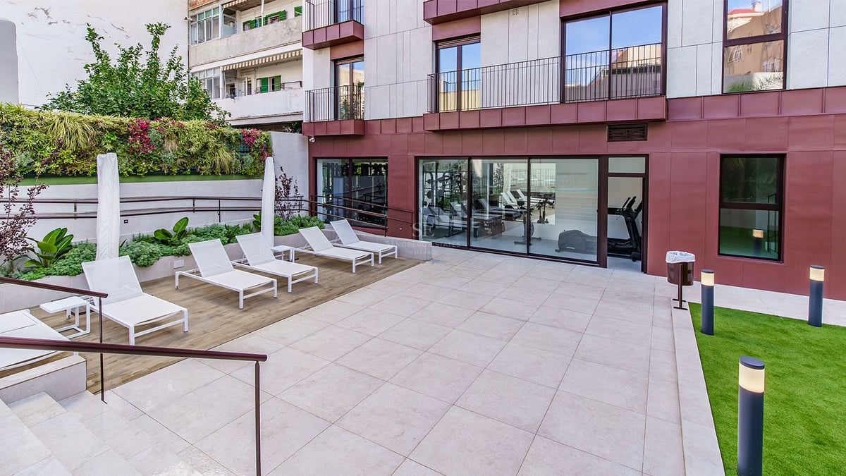 Terrasse extérieure avec chaises longues blanches, mur végétal et salle de sport vitrée en arrière-plan.