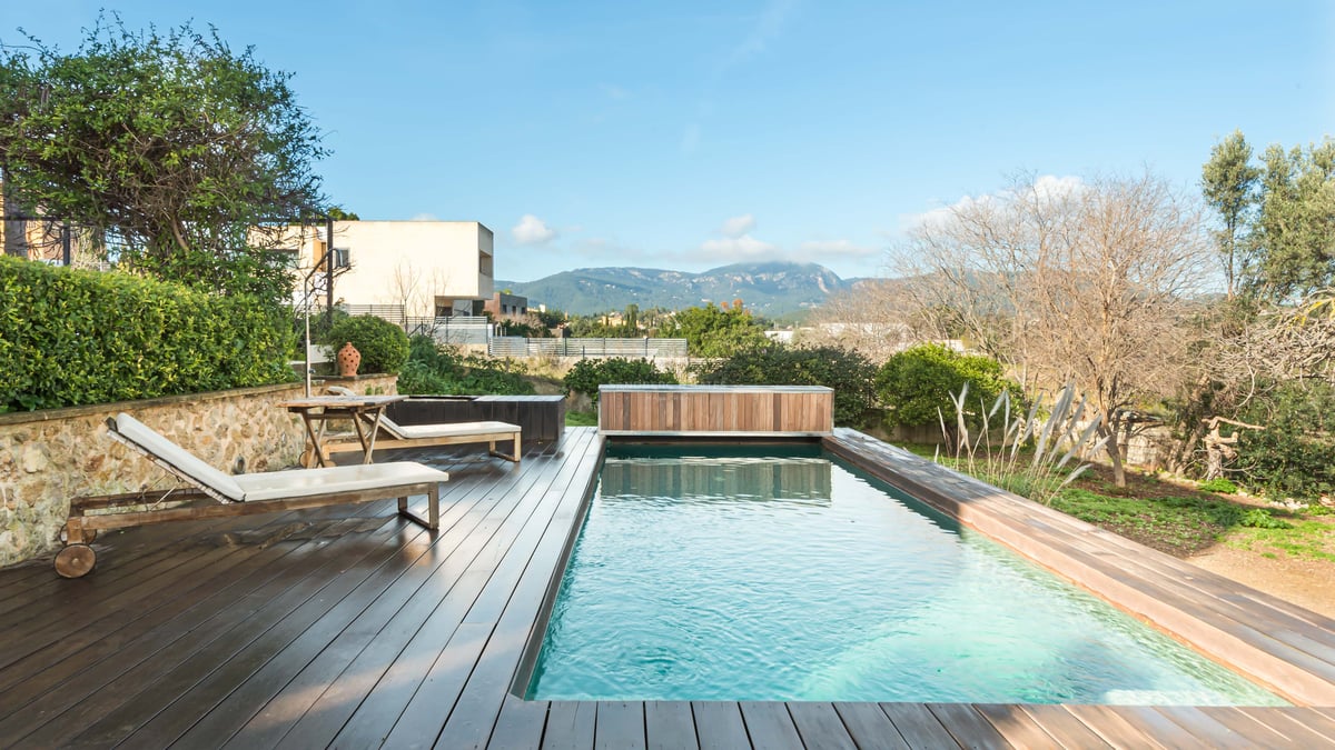 Piscine rectangulaire avec terrasse en bois sombre, bains de soleil blancs et vue panoramique sur les montagnes.