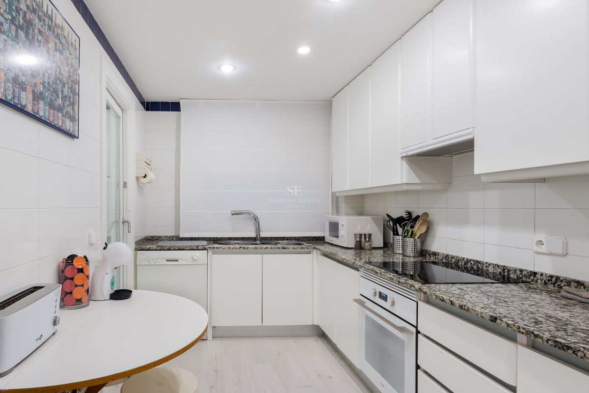 Cuisine moderne blanche avec plans de travail en granit, appareils intégrés et un petit coin petit-déjeuner.
