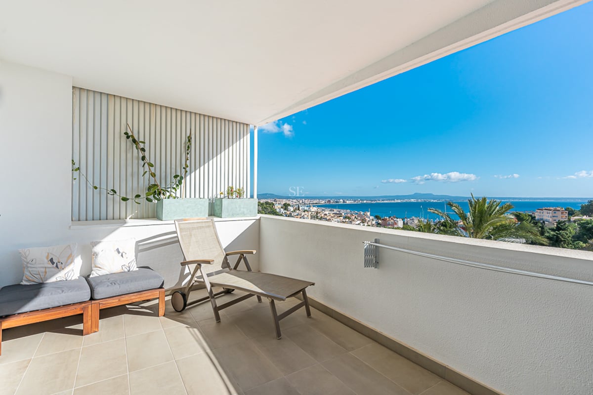 Grand balcon avec rambarde en verre, vue panoramique sur la mer et mobilier moderne de détente. Les plantes ajoutent une touche naturelle.