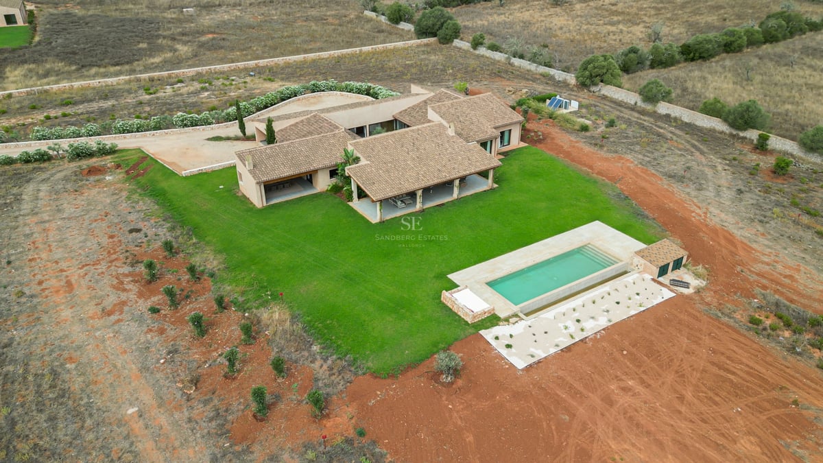 Vue aérienne d'une villa moderne avec toit en tuiles, pelouse verte et piscine rectangulaire à la campagne.