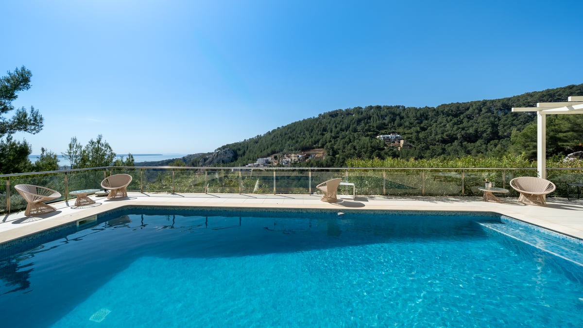 Piscine rectangulaire avec terrasse en pierre claire, garde-corps en verre et vue sur des collines verdoyantes.