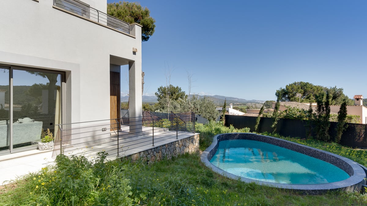 Villa blanche moderne avec piscine courbe en mosaïque bleue, base en pierre et vue sur la montagne par temps clair.