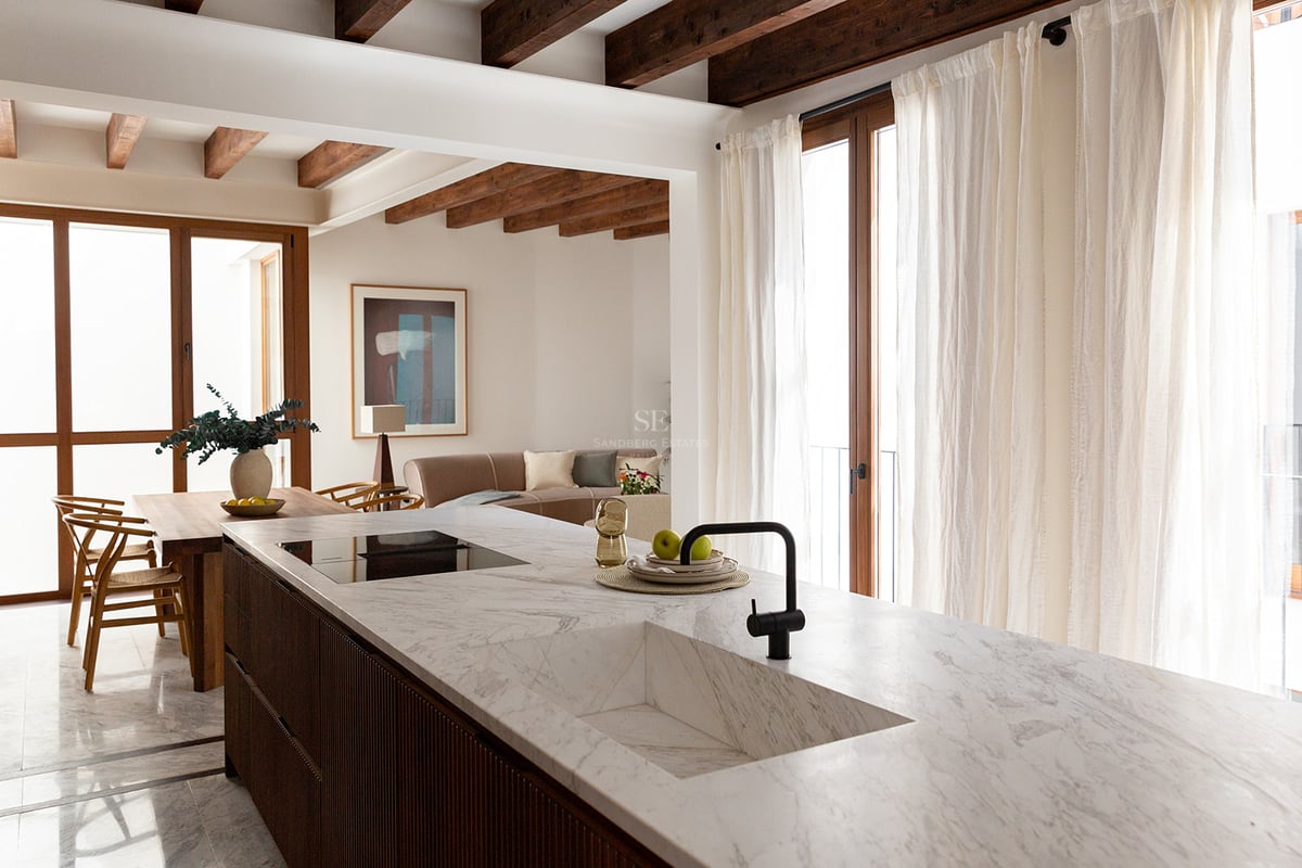Cocina moderna con isla de mármol blanco, fregadero integrado, muebles de madera oscura y vigas de madera vistas.
