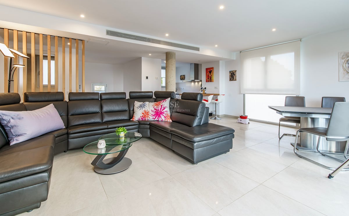 Salon spacieux avec un grand canapé en cuir noir, table basse en verre et coin repas moderne.