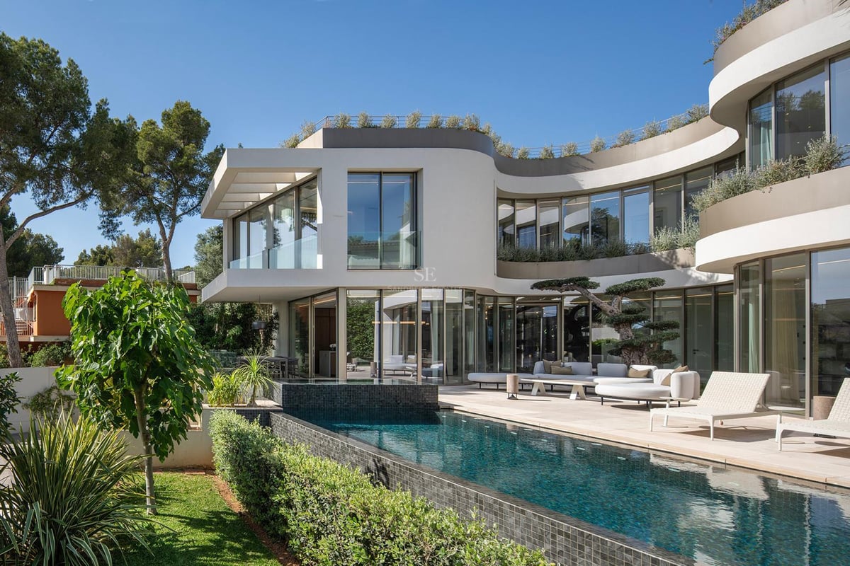 Villa blanche contemporaine aux murs courbes, piscine à débordement turquoise et salon extérieur sous un ciel bleu.
