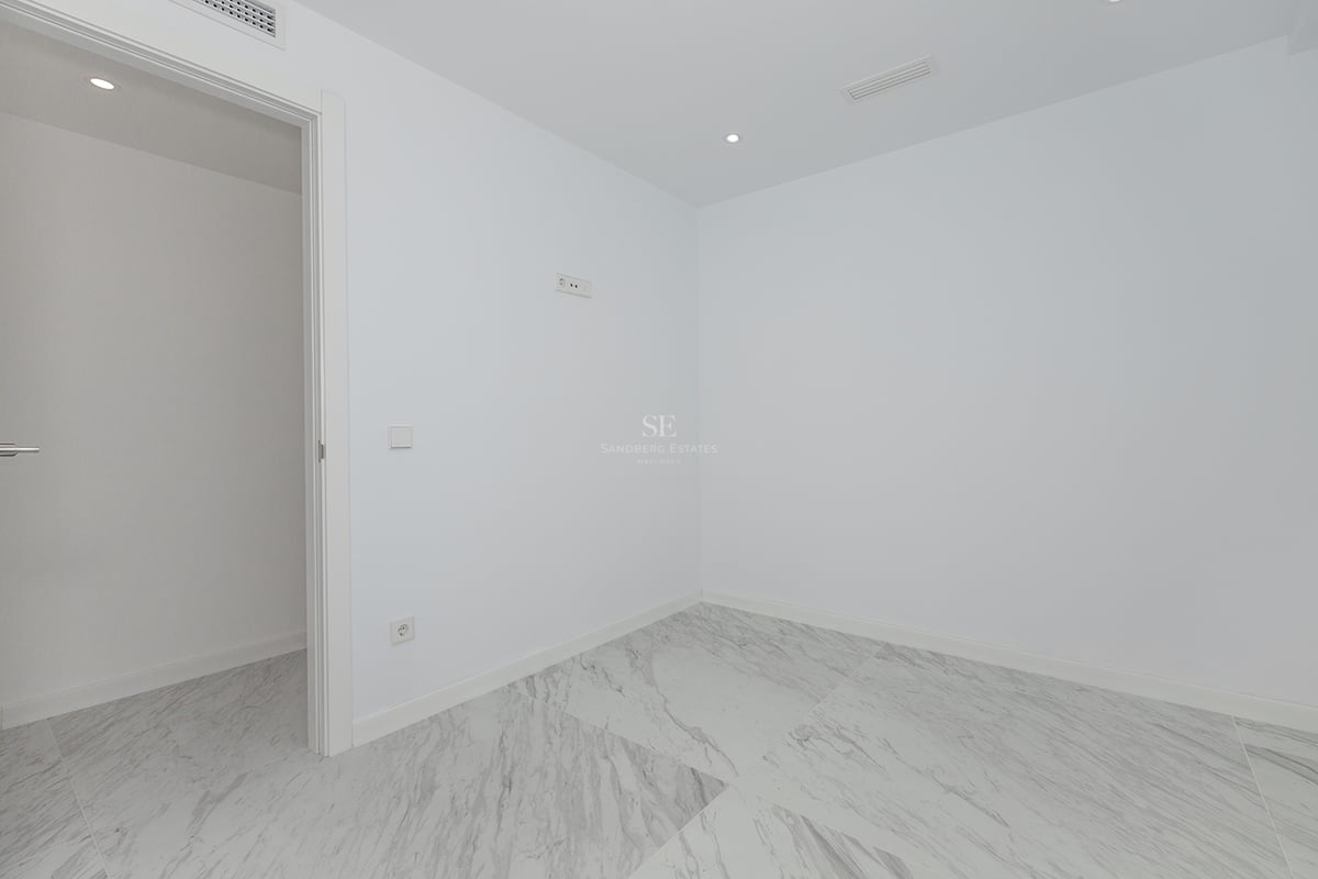 Pièce vide aux murs blancs avec carrelage en marbre grand format et éclairage LED intégré au plafond.