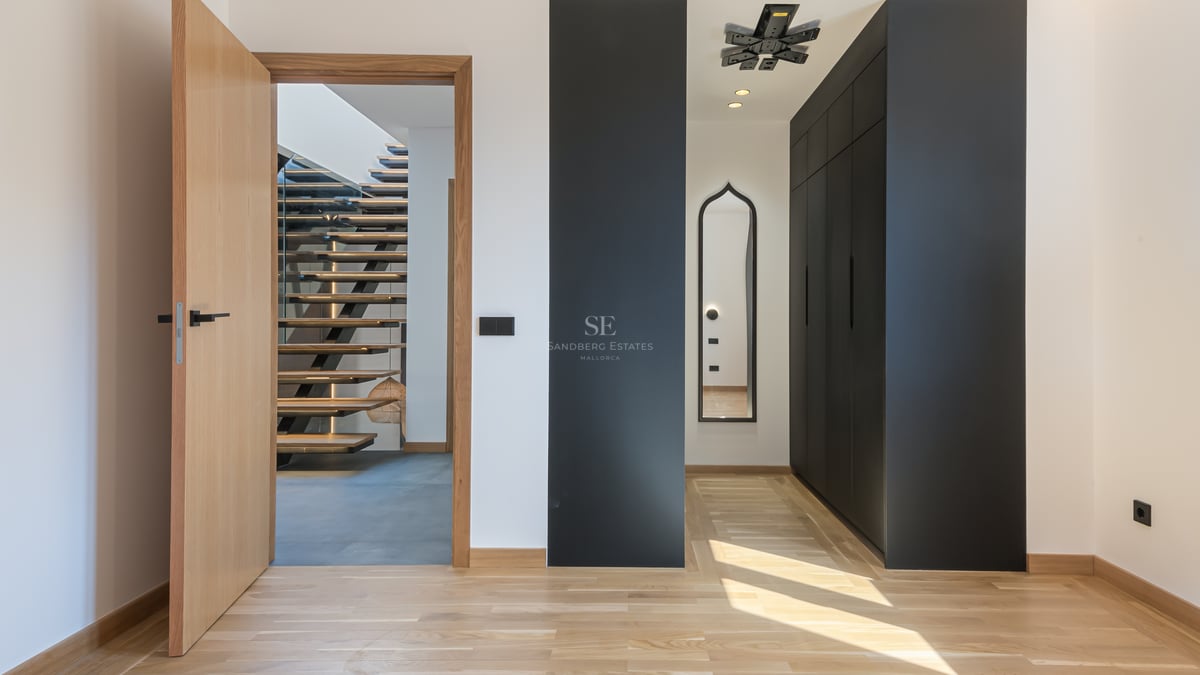 Couloir moderne avec parquet en bois, placards noirs intégrés et vue sur un escalier flottant en bois.