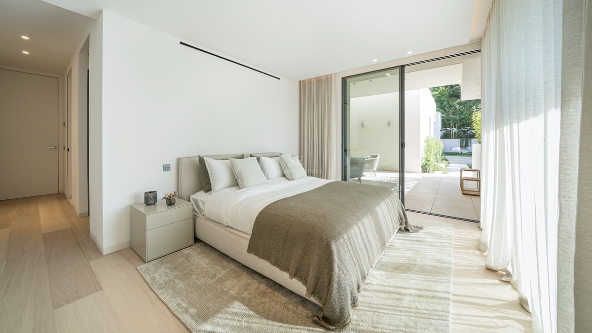 Chambre moderne avec grand lit, parquet clair et baies vitrées coulissantes ouvrant sur une terrasse privée.