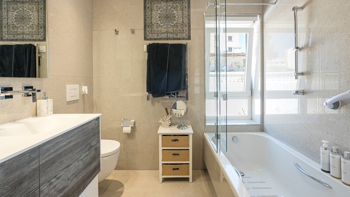 Salle de bain moderne avec baignoire blanche, paroi en verre, meuble en bois et carrelage mural effet pierre naturelle.