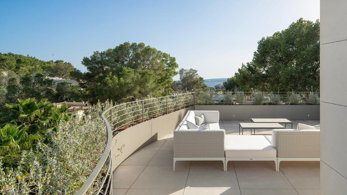 Terrasse moderne avec salon de jardin blanc, garde-corps métallique et vue sur les pins et la mer.