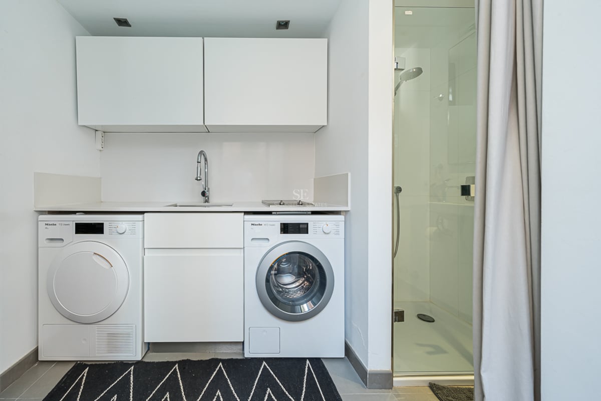Espace buanderie blanc avec lave-linge et sèche-linge Miele à côté d'une douche vitrée.
