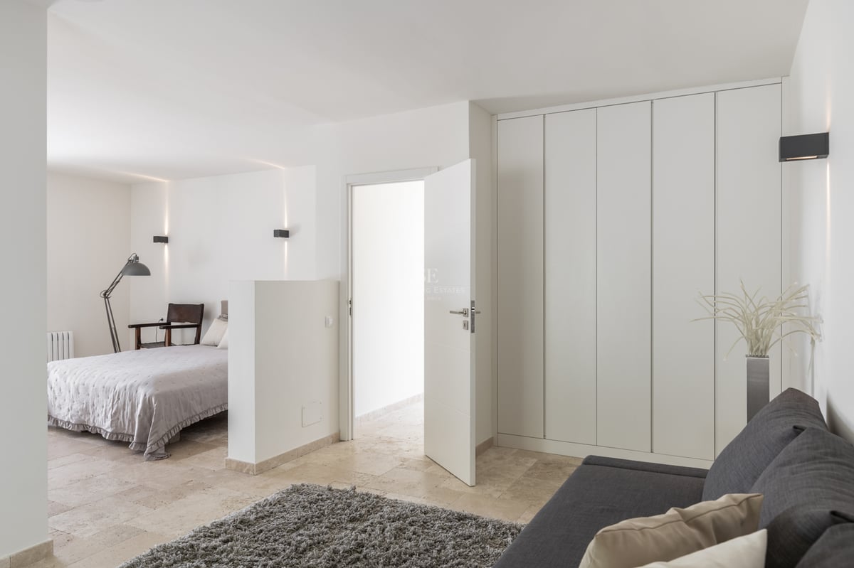 Chambre moderne avec carrelage en pierre beige, placards blancs, canapé gris et appliques murales minimalistes.