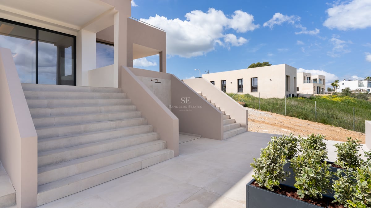 Escaliers en pierre naturelle menant à une villa moderne beige sous un ciel bleu.