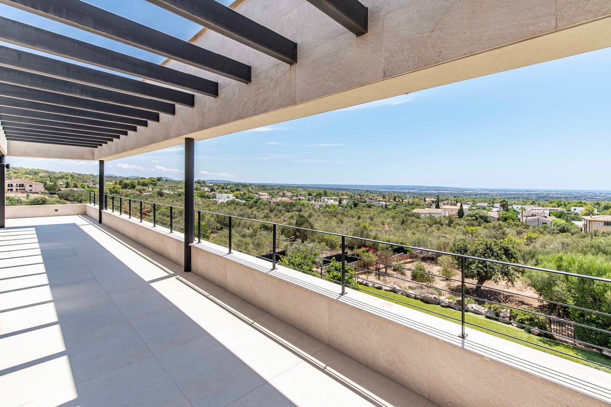 Grande terrasse moderne avec pergola à lames noires et vue sur une vallée verdoyante et le littoral.