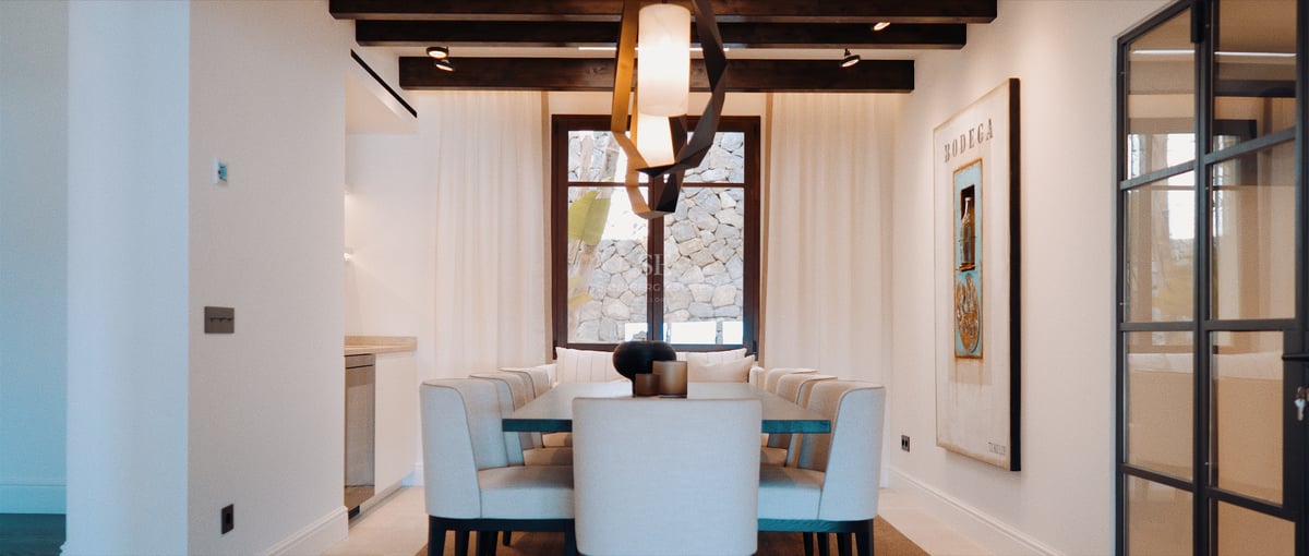 Salle à manger contemporaine avec chaises rembourrées, lustre sculptural et poutres en bois sombre au plafond.
