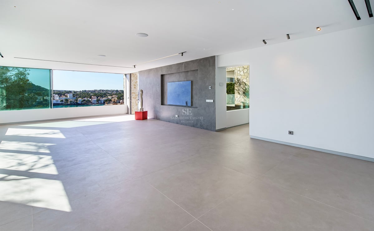 Grand salon minimaliste avec carrelage gris, murs blancs et baies vitrées offrant une vue panoramique sur la côte.