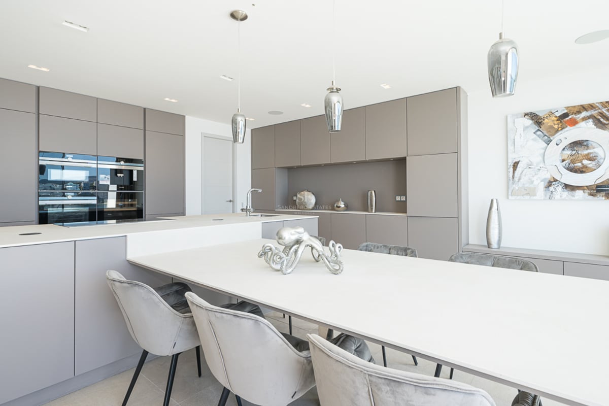 Cuisine contemporaine avec placards taupe, un grand îlot blanc et des chaises de salle à manger en velours gris.