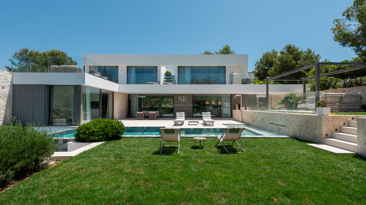 Vue arrière d'une villa contemporaine blanche sur deux niveaux avec piscine, jardin et murs en pierre naturelle.