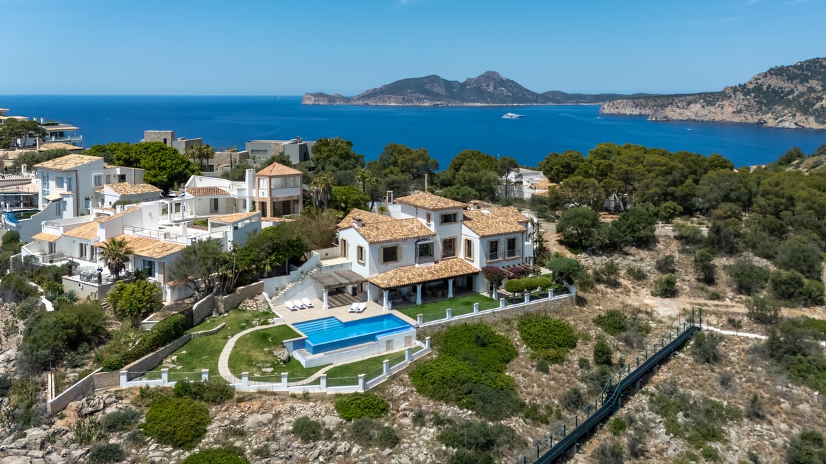 Vue aérienne d'une villa méditerranéenne blanche avec piscine surplombant la mer et les montagnes au loin.