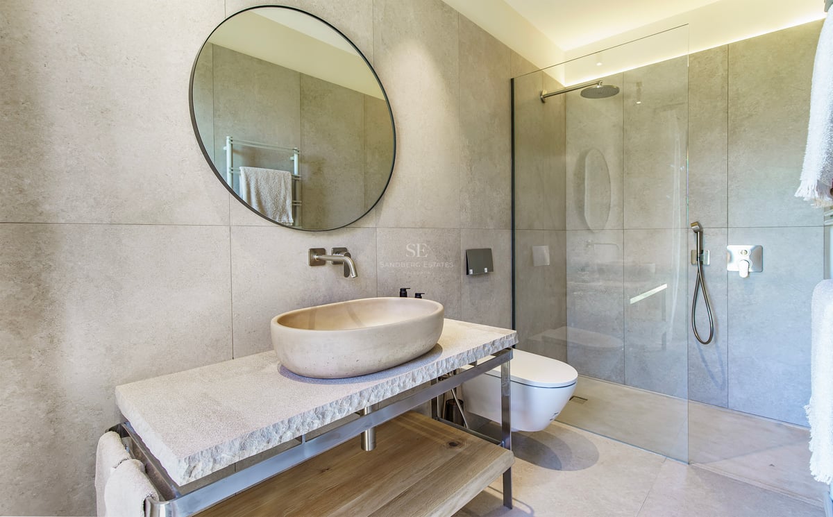 Baño contemporáneo con lavabo ovalado de piedra, espejo circular y ducha de cristal con azulejos de gran formato.