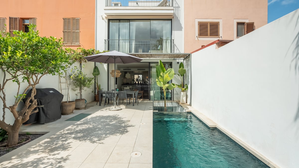 Cour extérieure moderne avec piscine, coin repas sous un parasol et murs blancs.