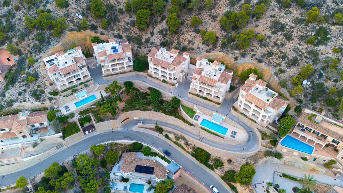 Vue aérienne d'appartements de luxe avec toits en terre cuite et piscines turquoise sur une colline verdoyante.