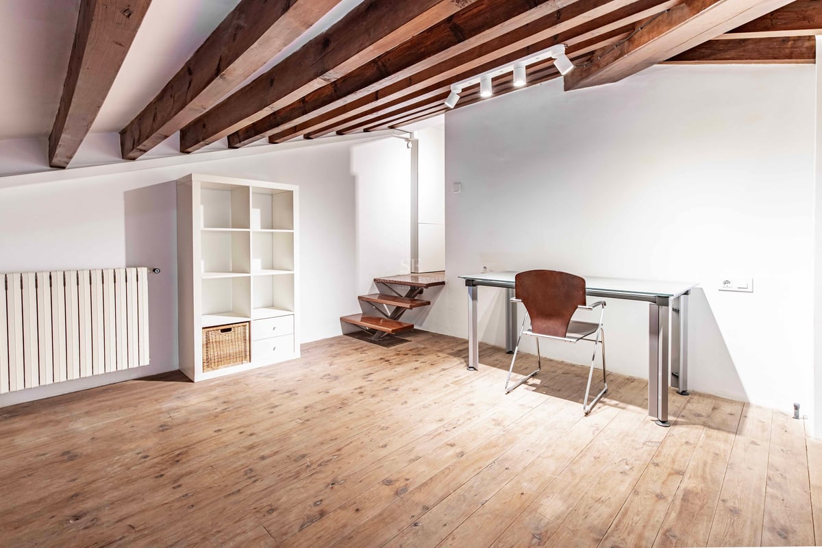 Bureau sous les toits avec poutres en bois apparentes, bureau en verre, parquet et étagère blanche minimaliste.