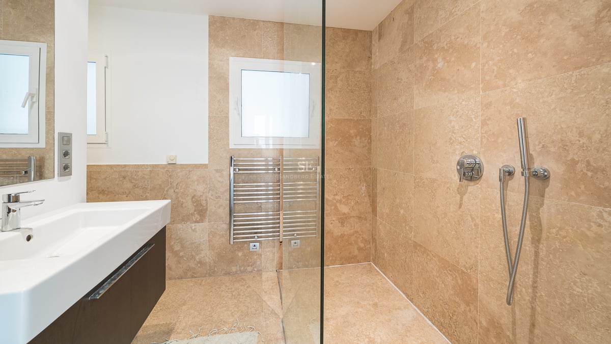 Salle de bain moderne avec carrelage en travertin beige, douche à l'italienne vitrée et sèche-serviettes.