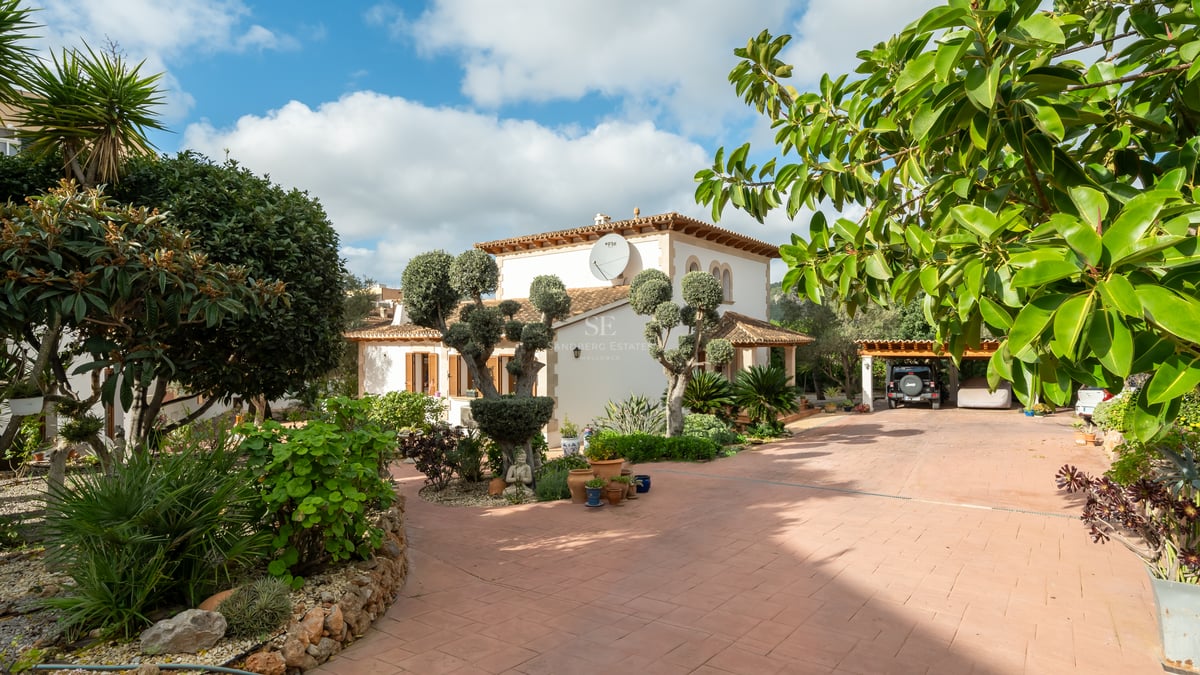 Villa méditerranéenne avec allée en terre cuite, oliviers taillés et parking couvert sous le soleil.