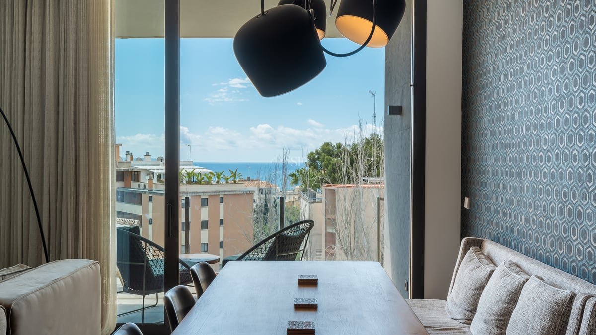 Salle à manger moderne avec table en bois, papier peint bleu et vue panoramique sur la mer Méditerranée.