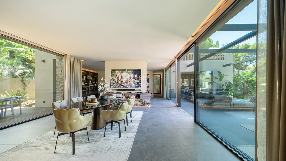 Salle à manger moderne et spacieuse avec baies vitrées, chaises beiges élégantes et vue sur un jardin ensoleillé.
