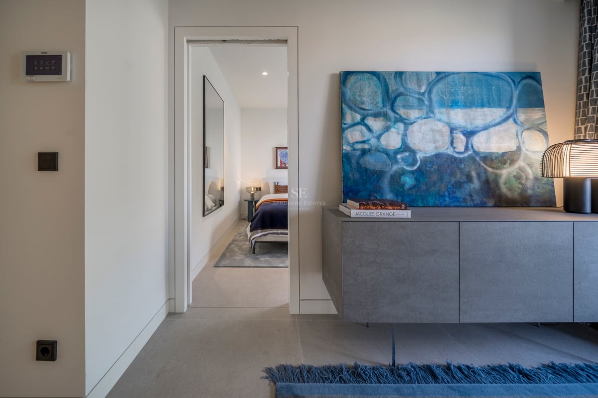 Buffet gris moderne avec peinture abstraite bleue et lampe design, ouvrant sur une chambre lumineuse.