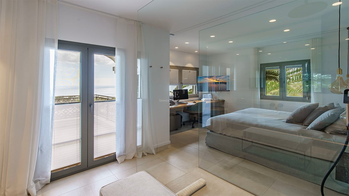Chambre moderne avec cloison en verre, coin bureau intégré et balcon donnant sur la mer.