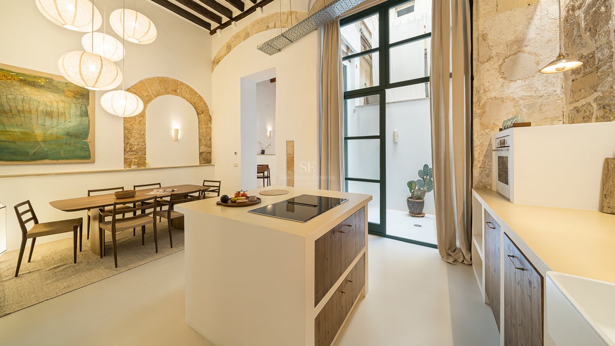 Cuisine moderne avec îlot central, arches en pierre apparente, plafonds en bois et lampes en papier près d'une salle à manger.