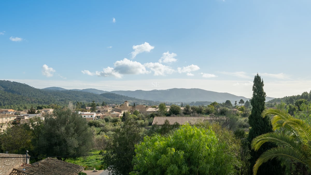 Vue surélevée d'un village méditerranéen aux toits de terre cuite, entouré de verdure et de montagnes verdoyantes.
