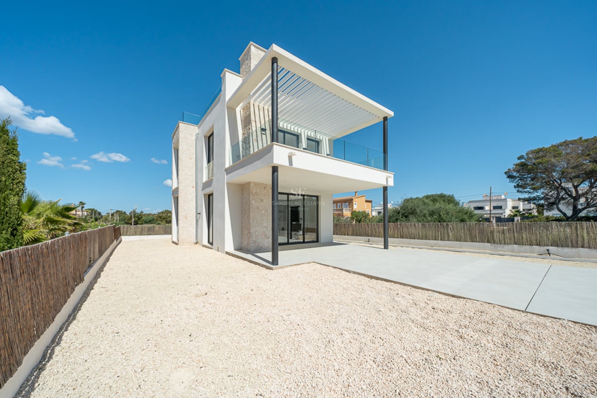 Villa moderne blanche de deux étages avec murs en pierre naturelle, grand balcon et cour en gravier sous un ciel bleu clair.