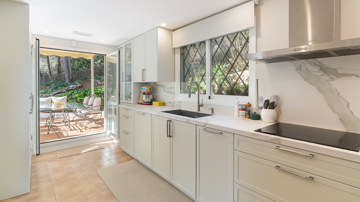 Cuisine lumineuse avec placards blancs, plans de travail en marbre et portes vitrées ouvrant sur une terrasse.