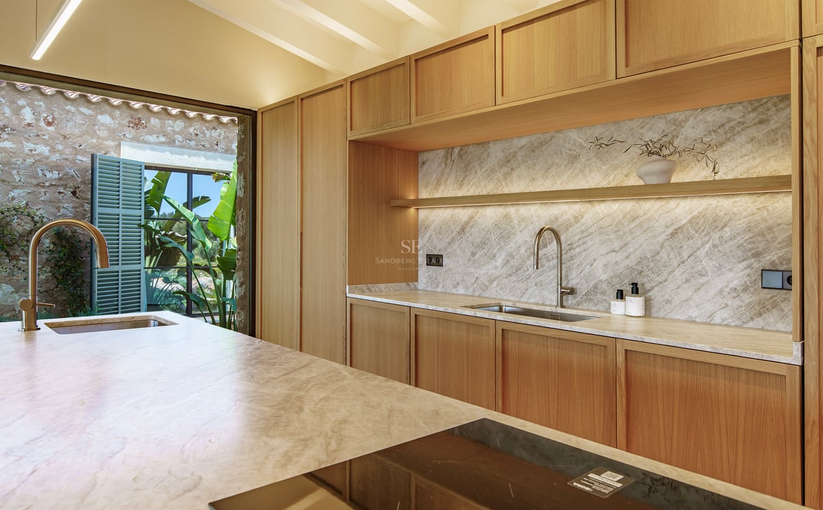 Cocina moderna con muebles de madera clara, salpicadero de mármol e isla con placa de inducción.