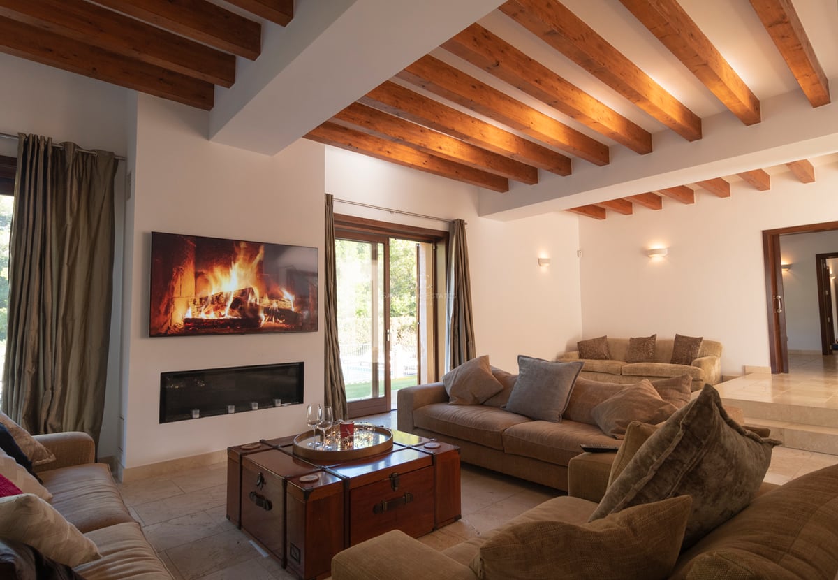 Grand salon avec plafond à poutres en bois, cheminée moderne, sol en pierre et accès direct au jardin.