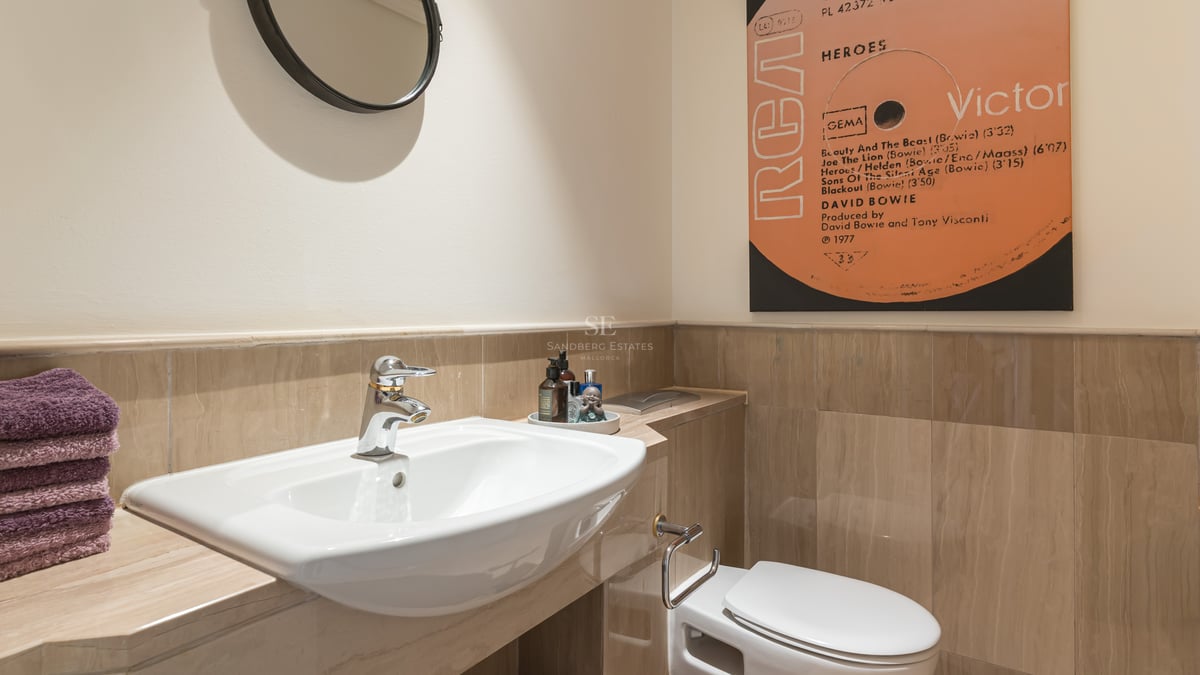 Salle de bains moderne avec lavabo en porcelaine, carrelage en marbre beige et décoration murale pop art.