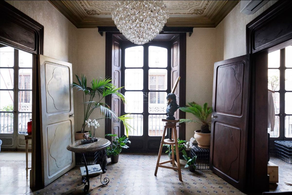 Gran entrada con puertas altas de madera, suelos de mosaico, una lámpara de cristal y plantas de interior.