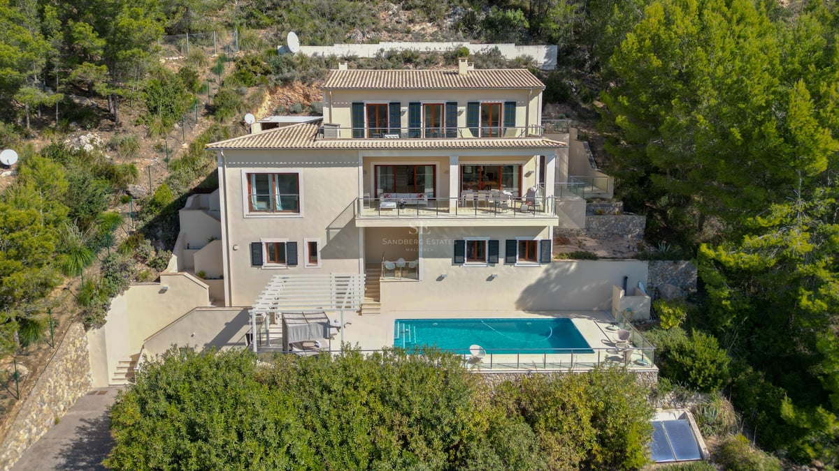 Vue aérienne d'une villa ocre de trois étages avec piscine, entourée d'une forêt de pins sur une colline.