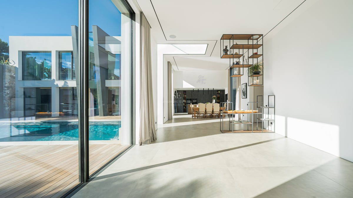 Salon lumineux à aire ouverte avec sols blancs, baies vitrées et vue sur une piscine privée.