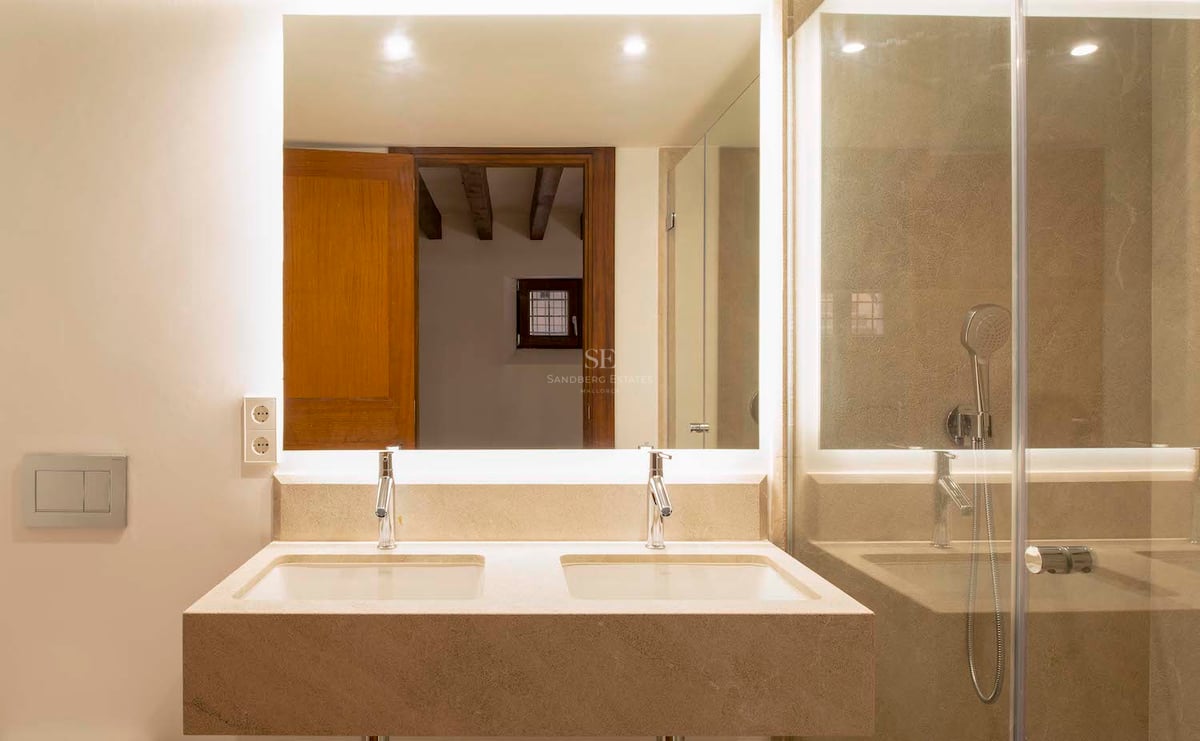 Salle de bain avec double vasque en pierre, grand miroir rétroéclairé et paroi de douche en verre.