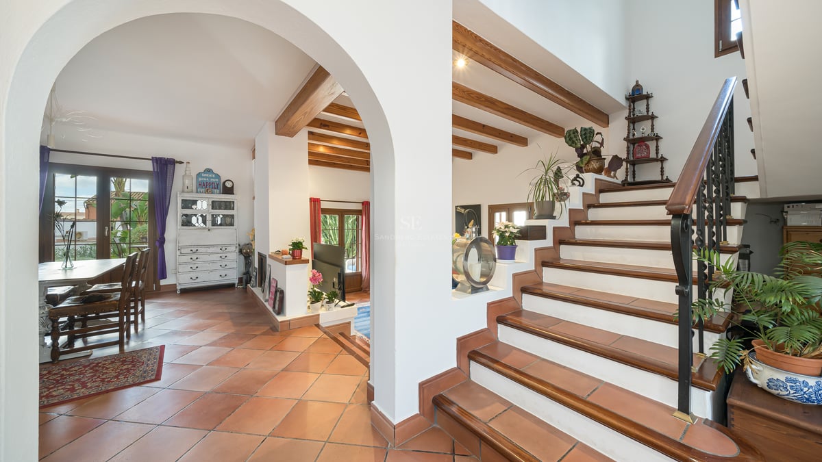 Vue intérieure avec sols en terre cuite, arche, poutres en bois au plafond et escalier en fer forgé.
