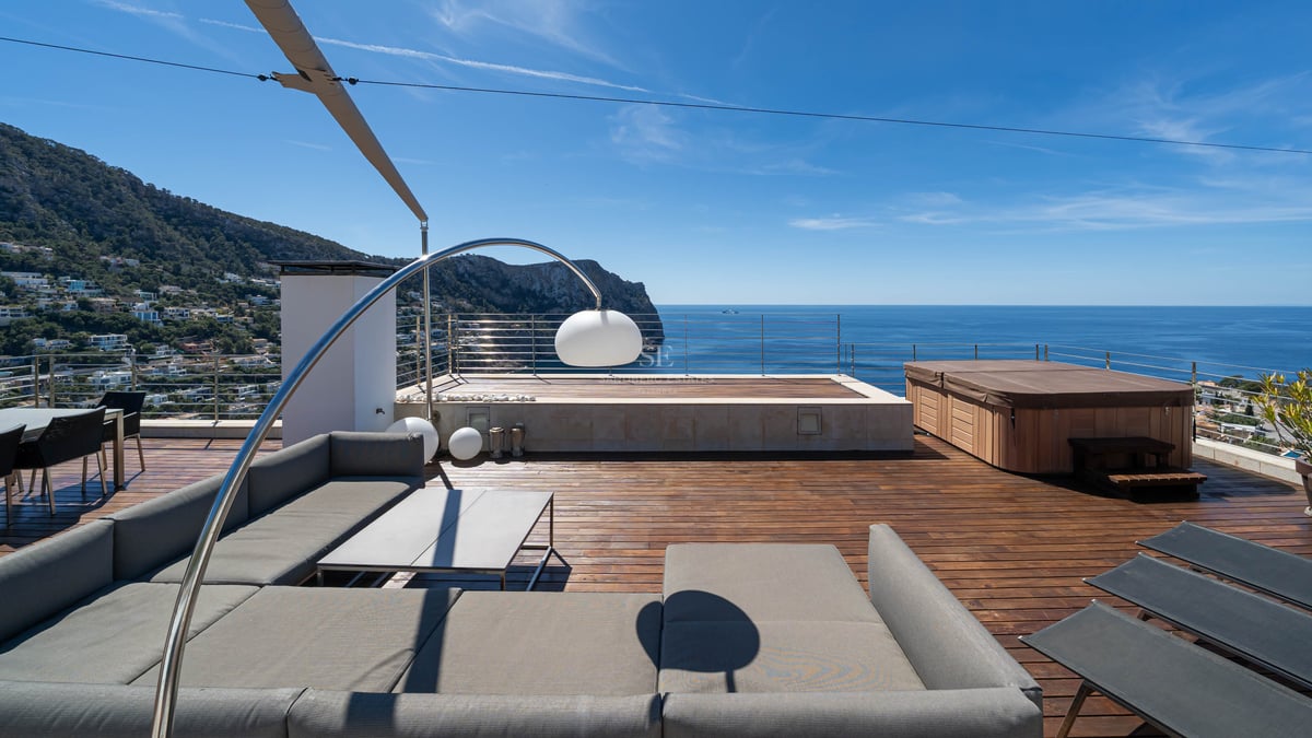 Toit-terrasse moderne avec canapé gris, terrasse en bois et jacuzzi surplombant la mer Méditerranée et les montagnes.