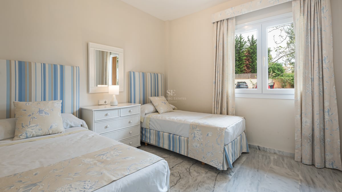 Chambre avec deux lits jumeaux, linge bleu et blanc, commode blanche et sol en marbre poli.