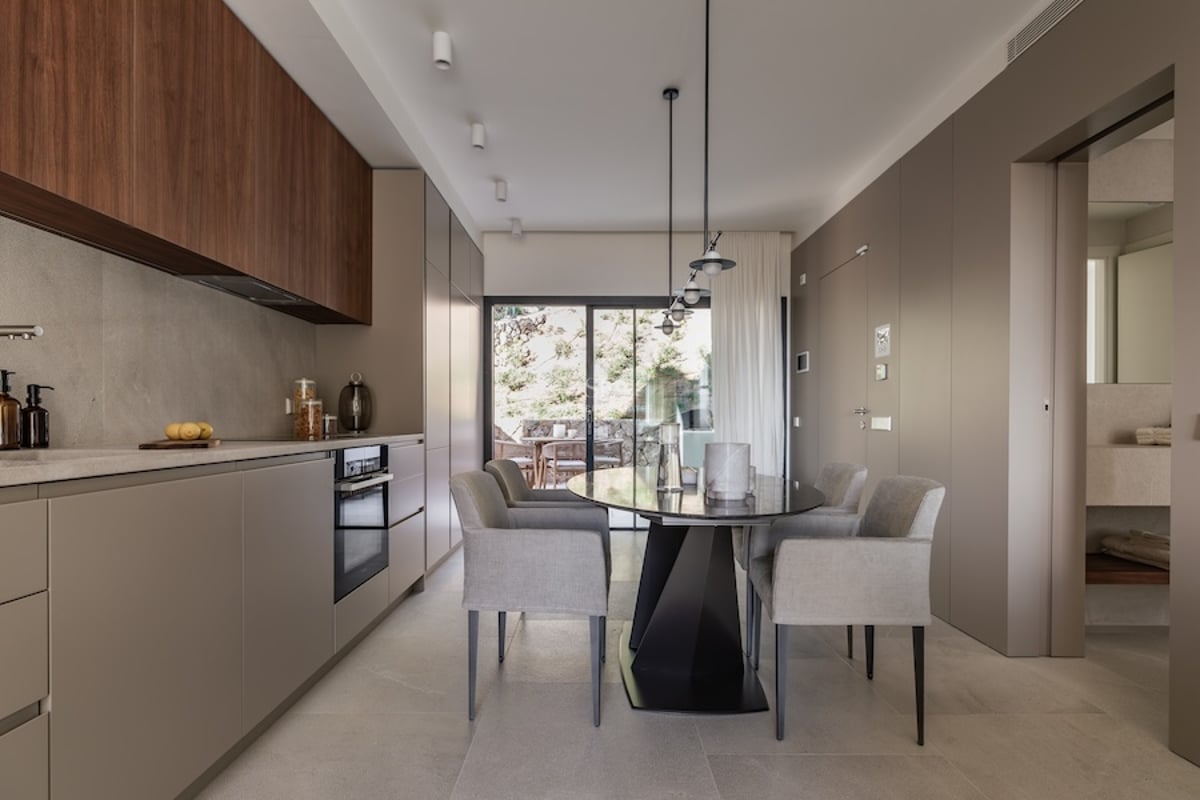 Cuisine minimaliste avec placards taupe et bois, table à manger grise et accès terrasse par de grandes baies vitrées.